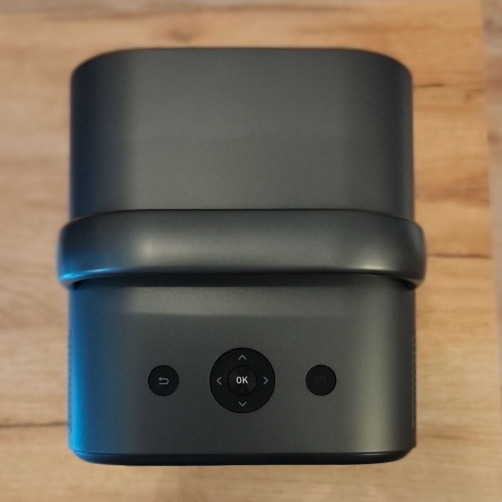 Widok z góry na obudowę projektora ETOE Seal Pro, pokazujący fizyczny panel sterowania z przyciskami kierunkowymi, przyciskiem zasilania i cofania, umieszczony pod rączką transportową