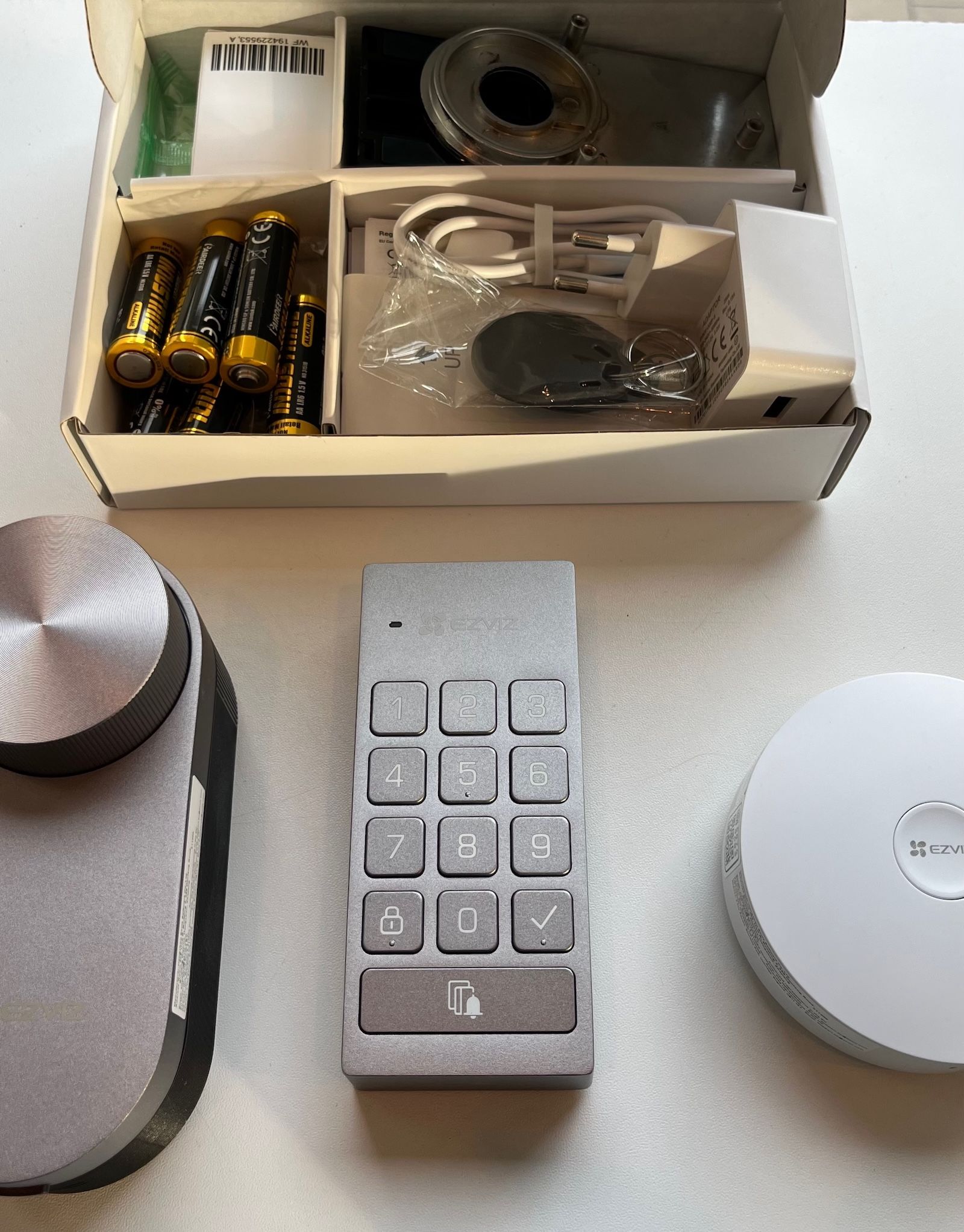 Rozpakowany zestaw EZVIZ DL01 Pro prezentujący zamek, klawiaturę, bramkę oraz pudełko z akcesoriami