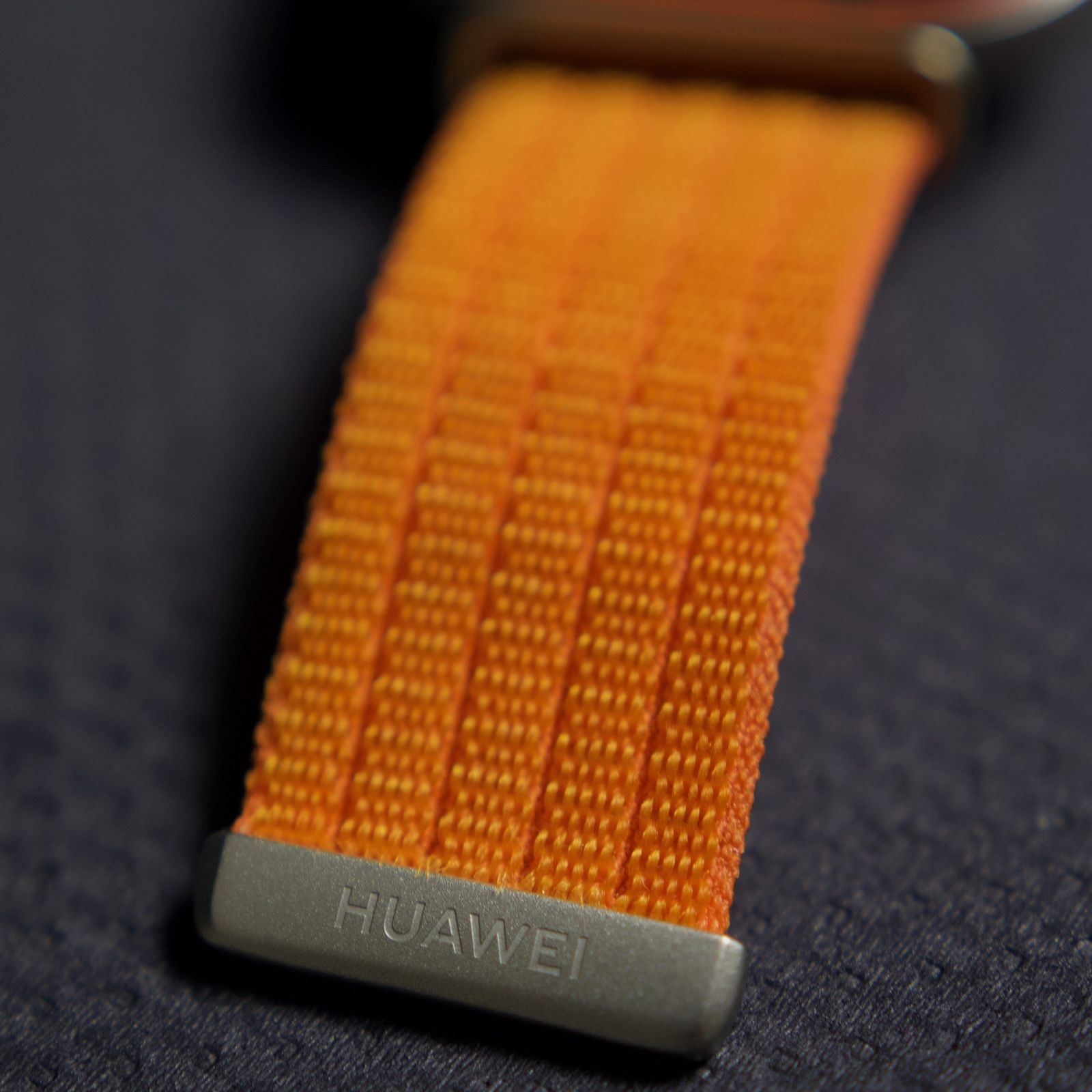 Detal zapięcia z logo na pomarańczowym pasku zegarka Huawei Watch Fit 5 Pro