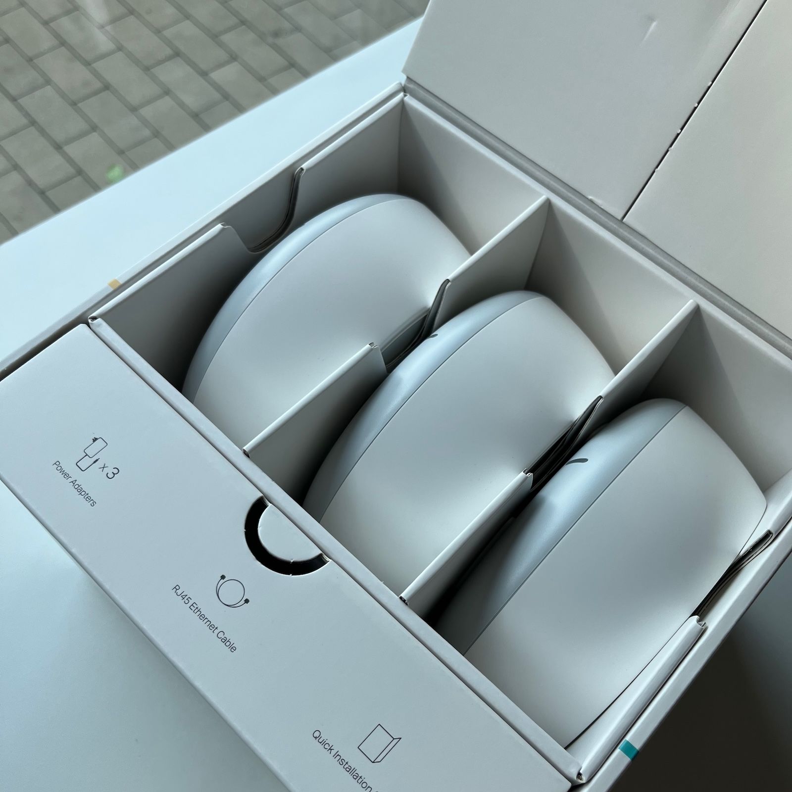 Otwarte pudełko z zestawem trzech routerów TP-Link Deco oraz wyraźnymi nadrukami oznaczającymi dołączone akcesoria