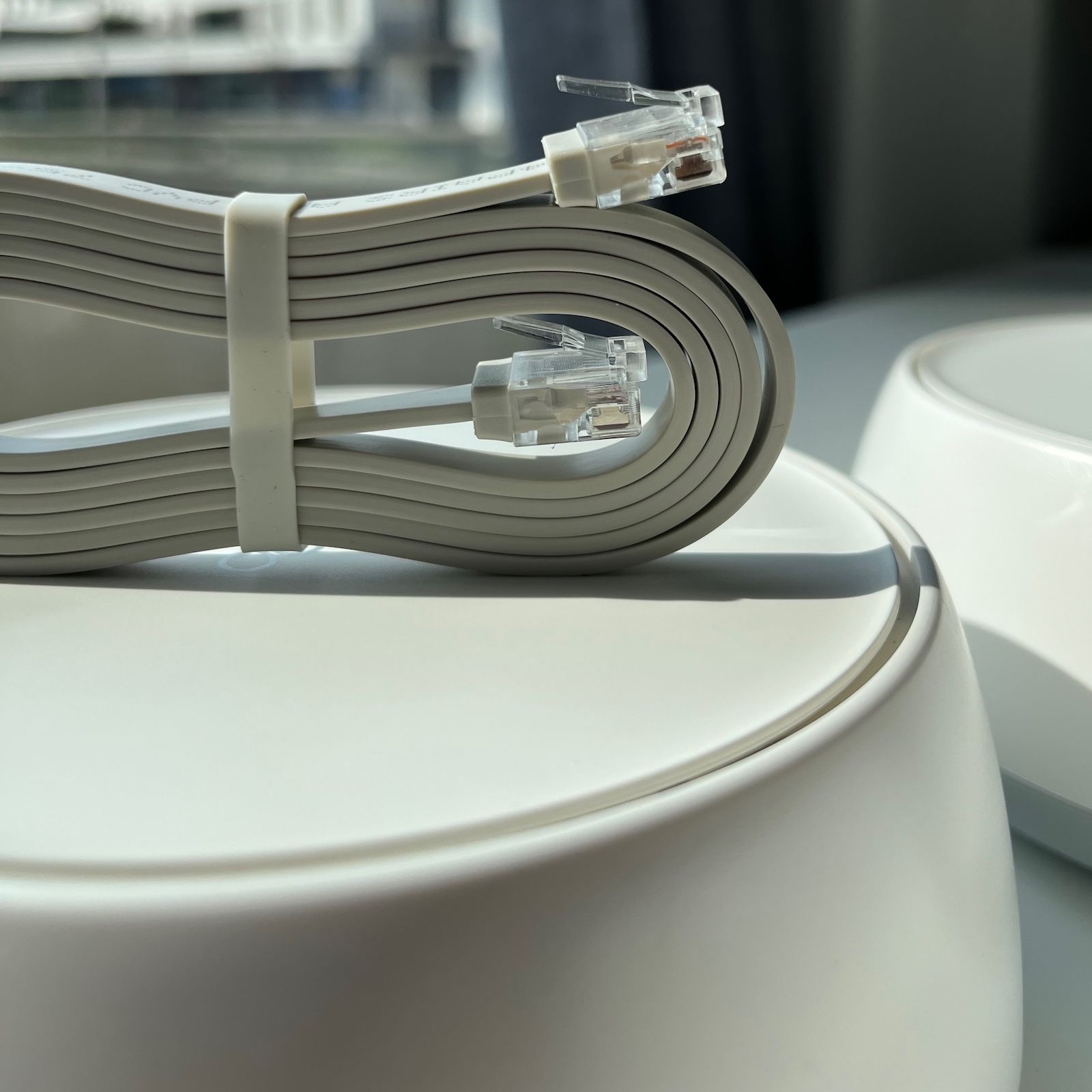 Płaski kabel Ethernet ze złączami RJ45 leżący luźno na białej obudowie routera TP-Link Deco