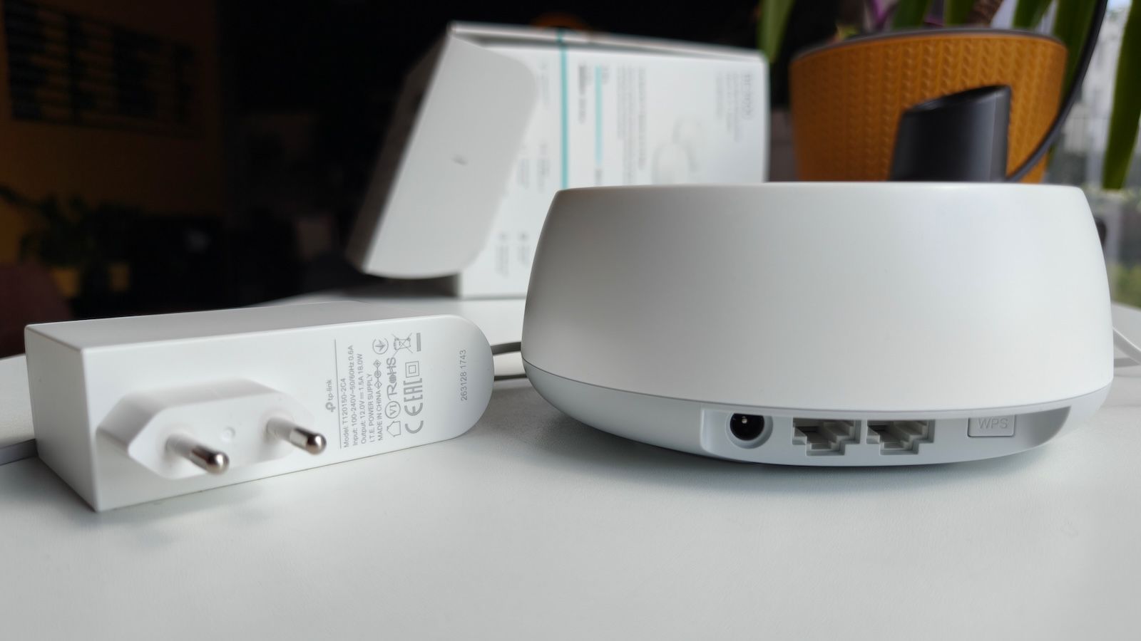 Tył modułu TP-Link Deco BE3600 z widocznymi portami, przyciskiem WPS i ładowarką obok