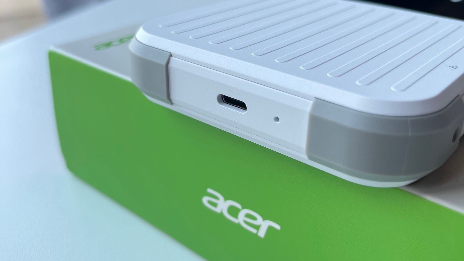 Zbliżenie na dolną krawędź routera Acer Connect M6E leżącego na zielonym pudełku, z widocznym portem USB-C i gumowymi osłonami narożników